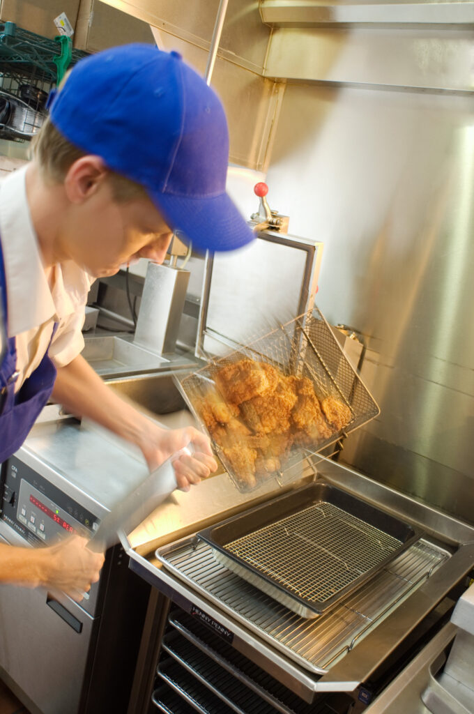 Chef pouring fried chicken onto pan
