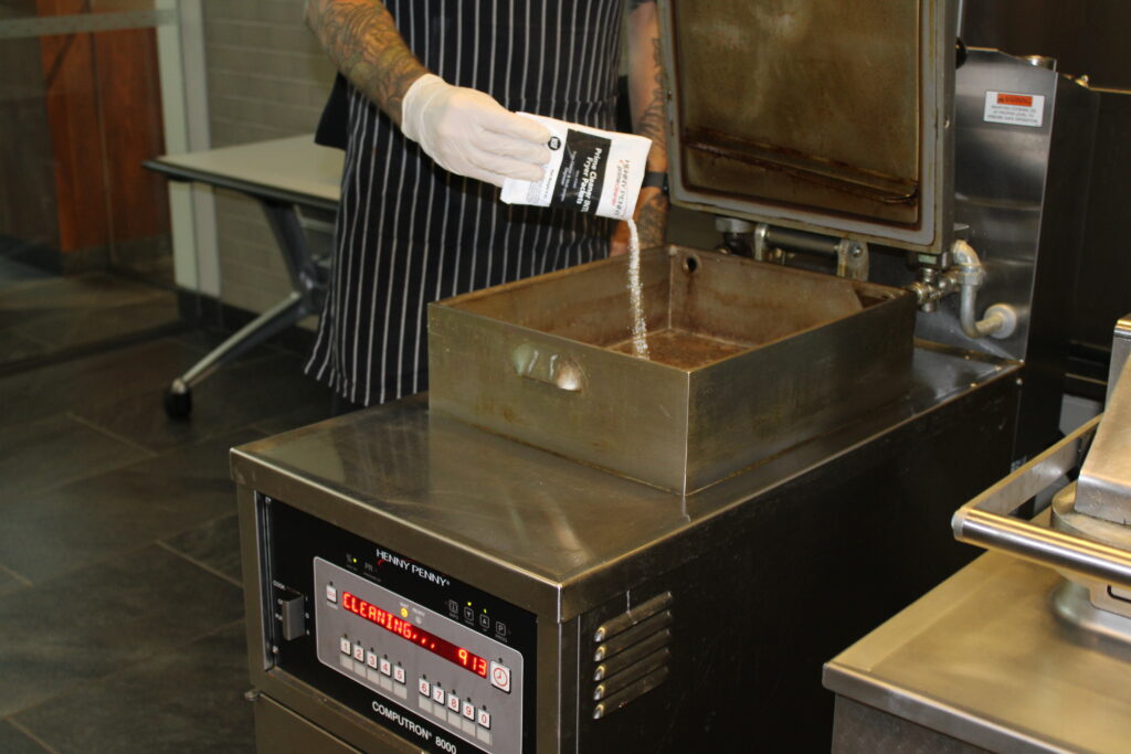 Team member performing routine commercial fryer oil maintenance