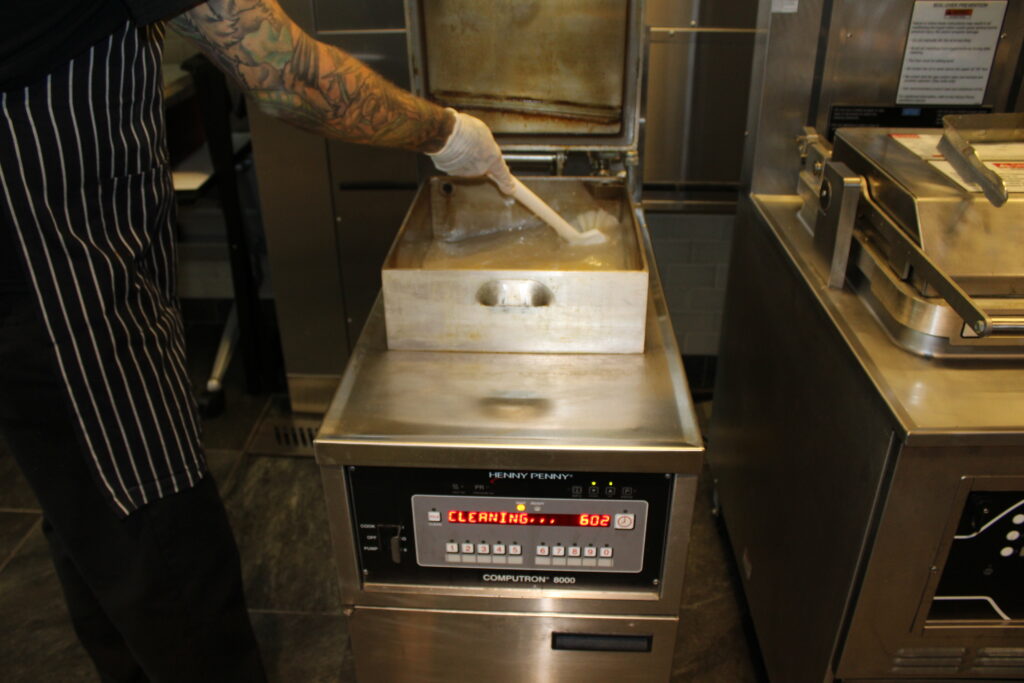 Team member performing routine commercial fryer oil maintenance
